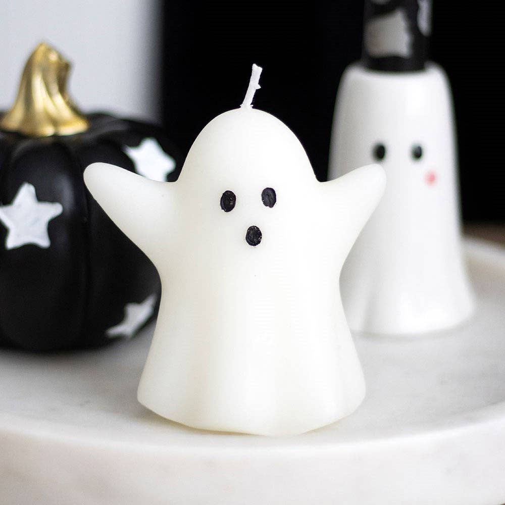 Ghost-shaped candle on a marble surface with pumpkins in the background