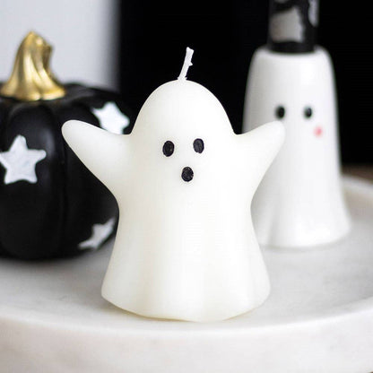 Ghost-shaped candle on a marble surface with pumpkins in the background