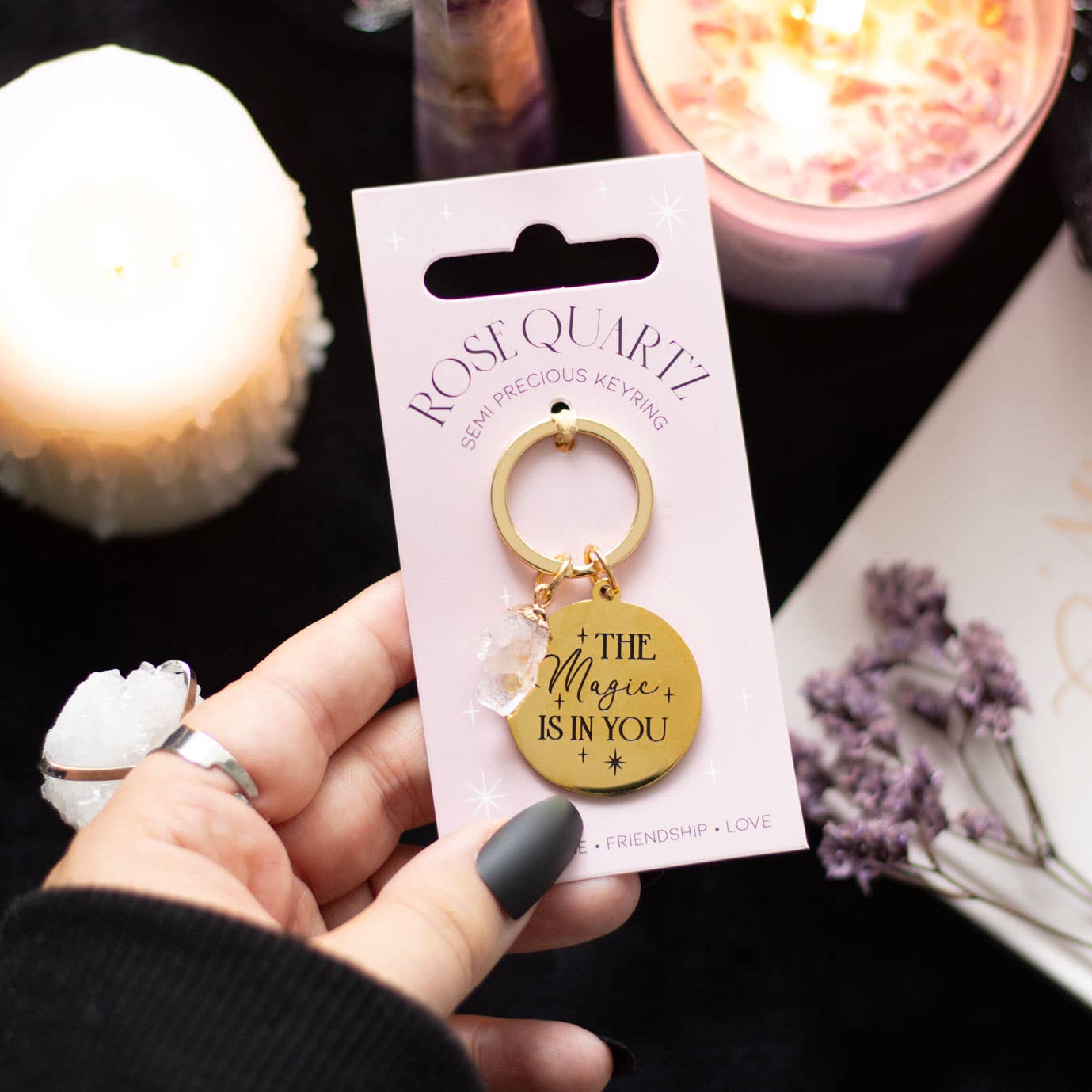Keychain with 'The Magic is in You' message held by a hand, with packaging and candles in the background.
