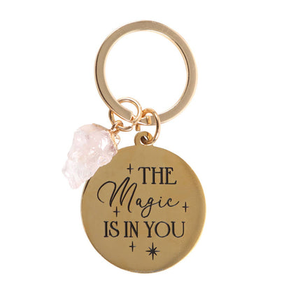 Gold keychain with 'The Magic is in You' text and pink crystal charm on a white background