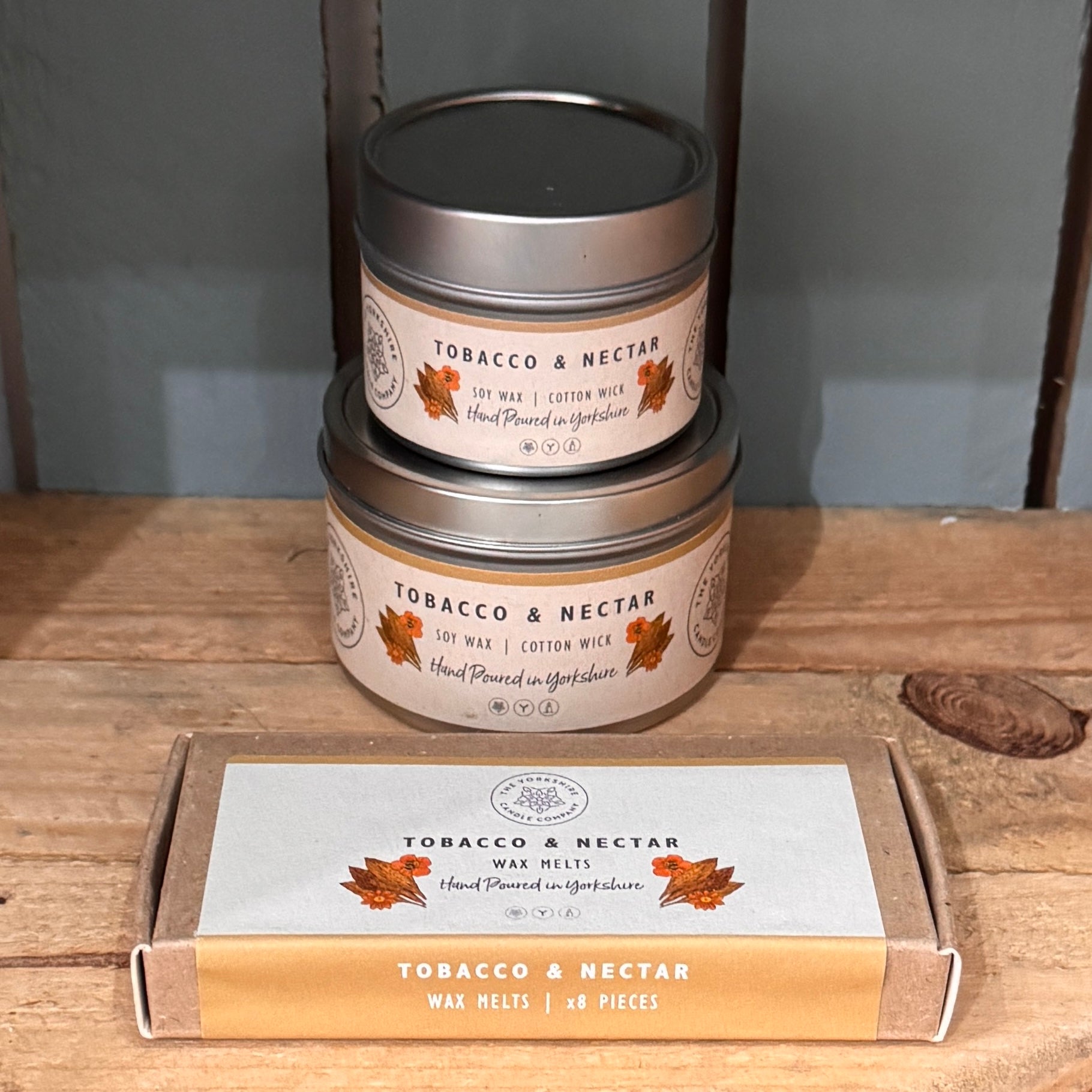 Two tins and a box of Tobacco & Nectar wax melts on a wooden surface.