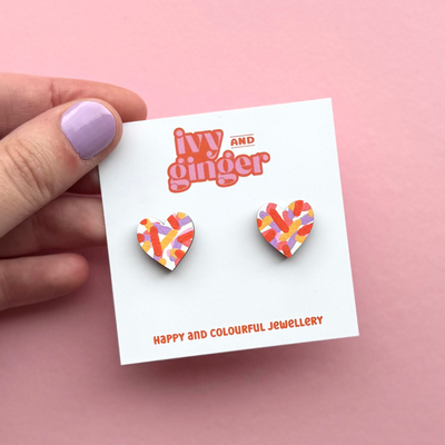 Heart-shaped earrings on a 'Ivy and Ginger' branded card against a pink background