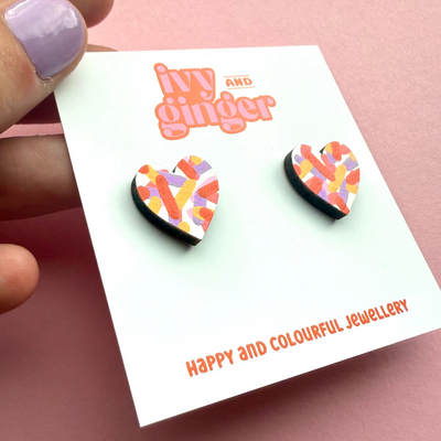 Colorful heart-shaped earrings on a 'ivy and ginger' branded card with a pink background.