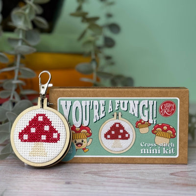 Cross-stitch keychain and kit with 'You're a Fungi!' text on a wooden surface.